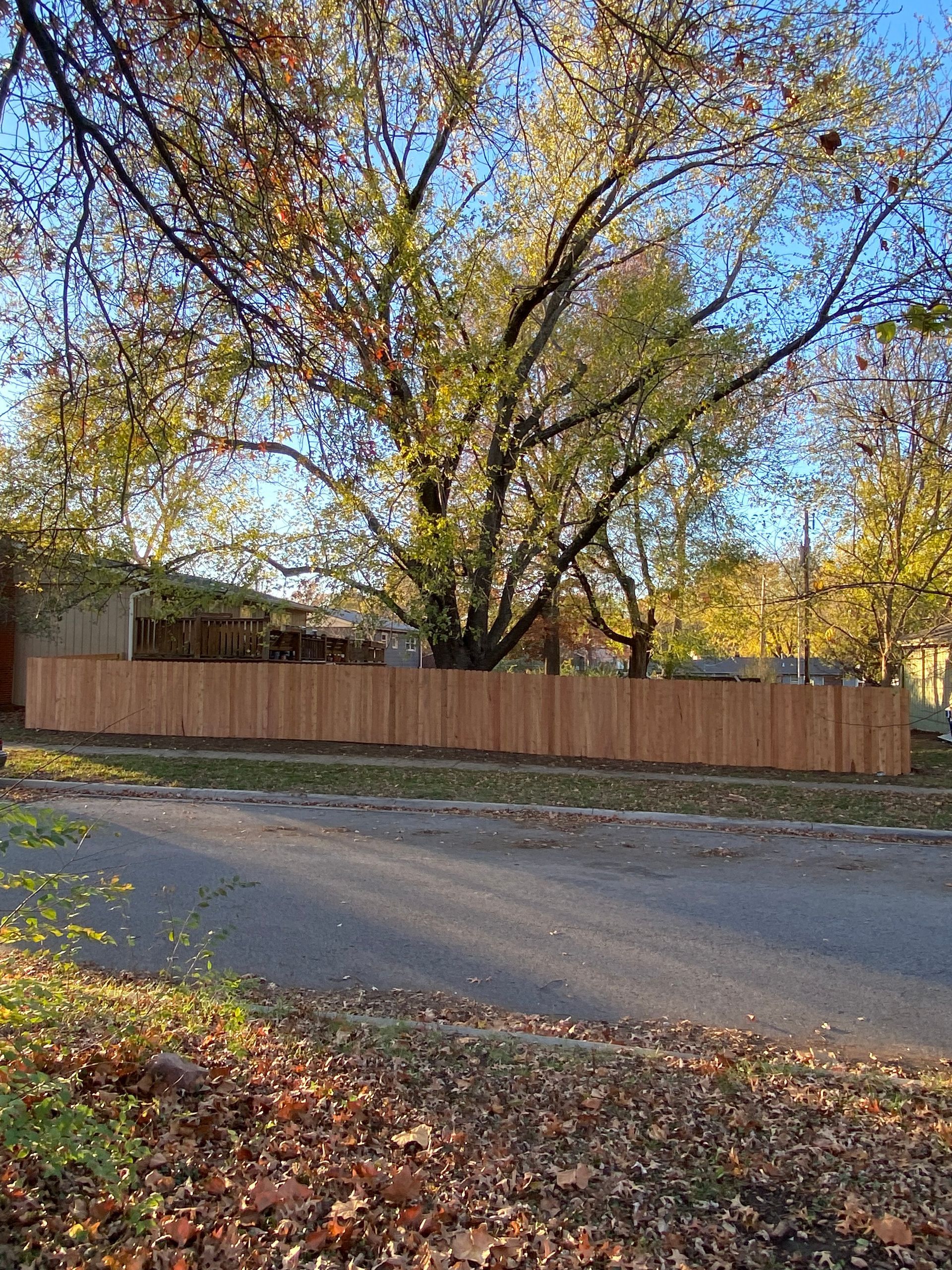 A wooden fence is surrounded by trees and leaves on the side of the road.