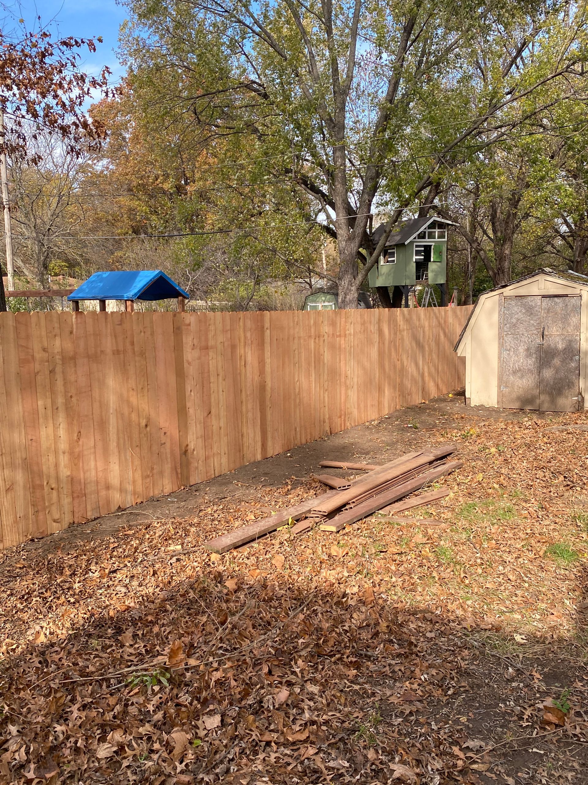 A wooden fence is surrounded by leaves in a backyard.