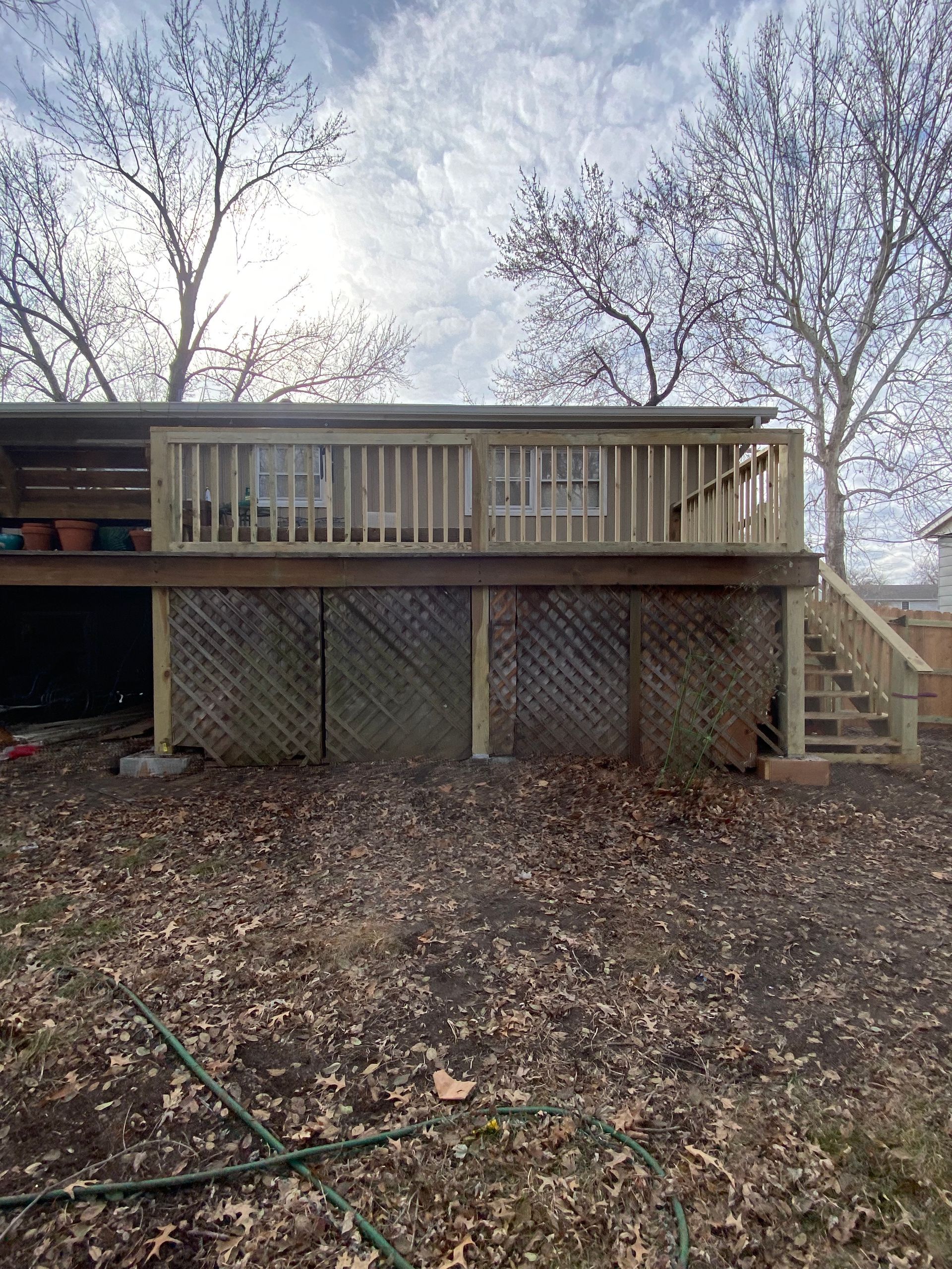 A large wooden deck with stairs leading up to it is in the backyard of a house.