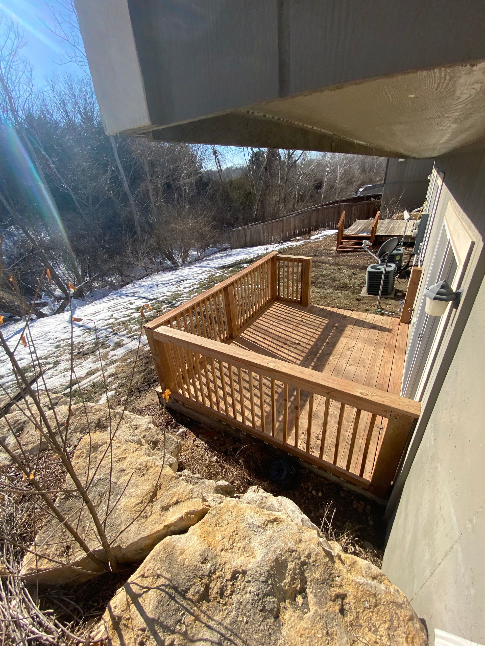 A wooden deck is sitting on top of a rocky hill next to a house.