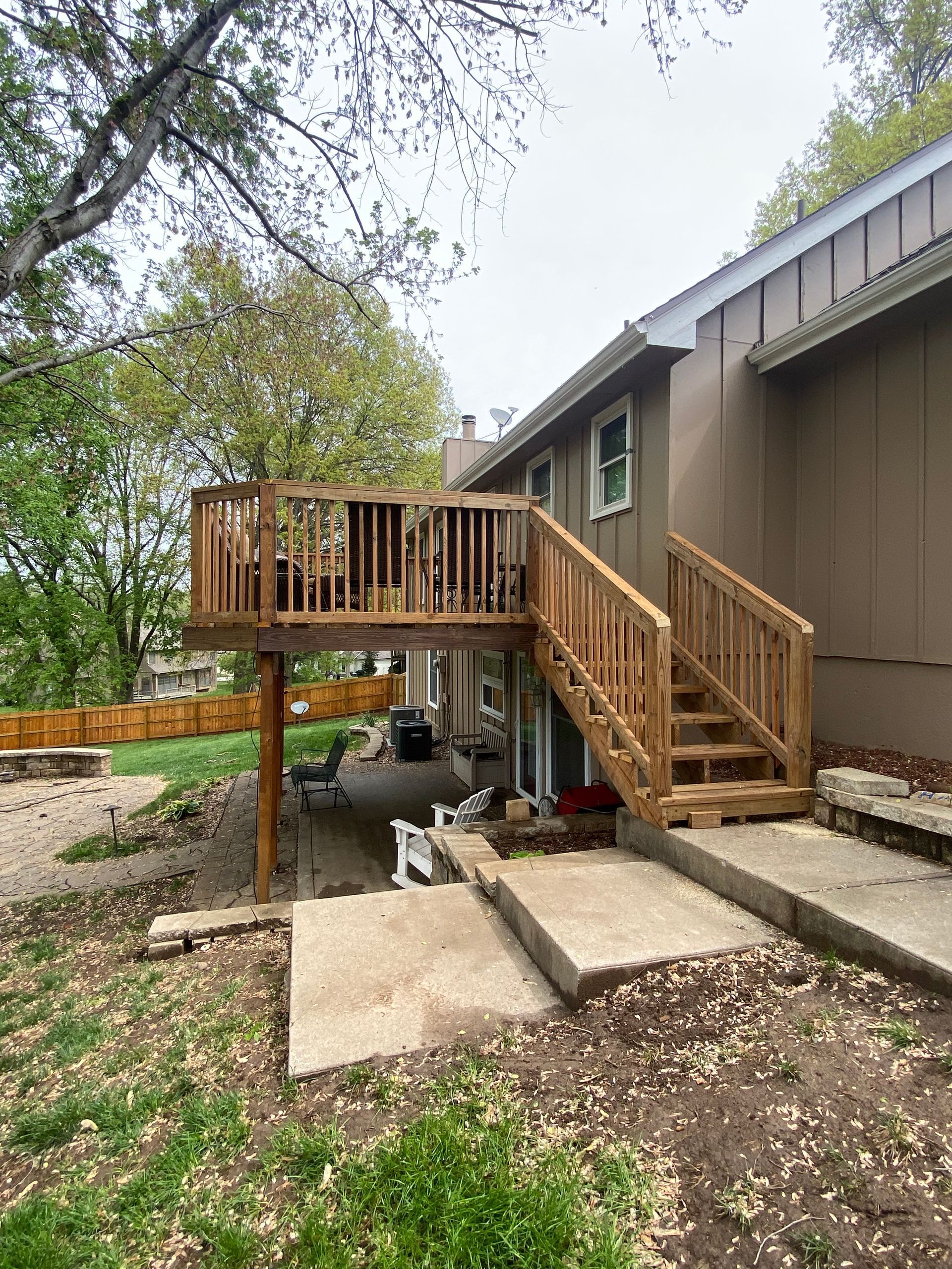 A wooden deck with stairs leading up to it is in the backyard of a house.