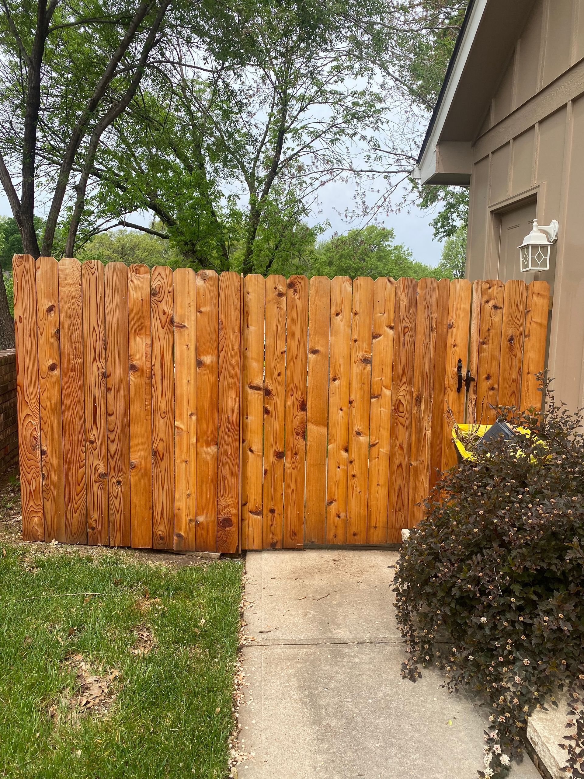 A wooden fence is sitting next to a sidewalk in front of a house.