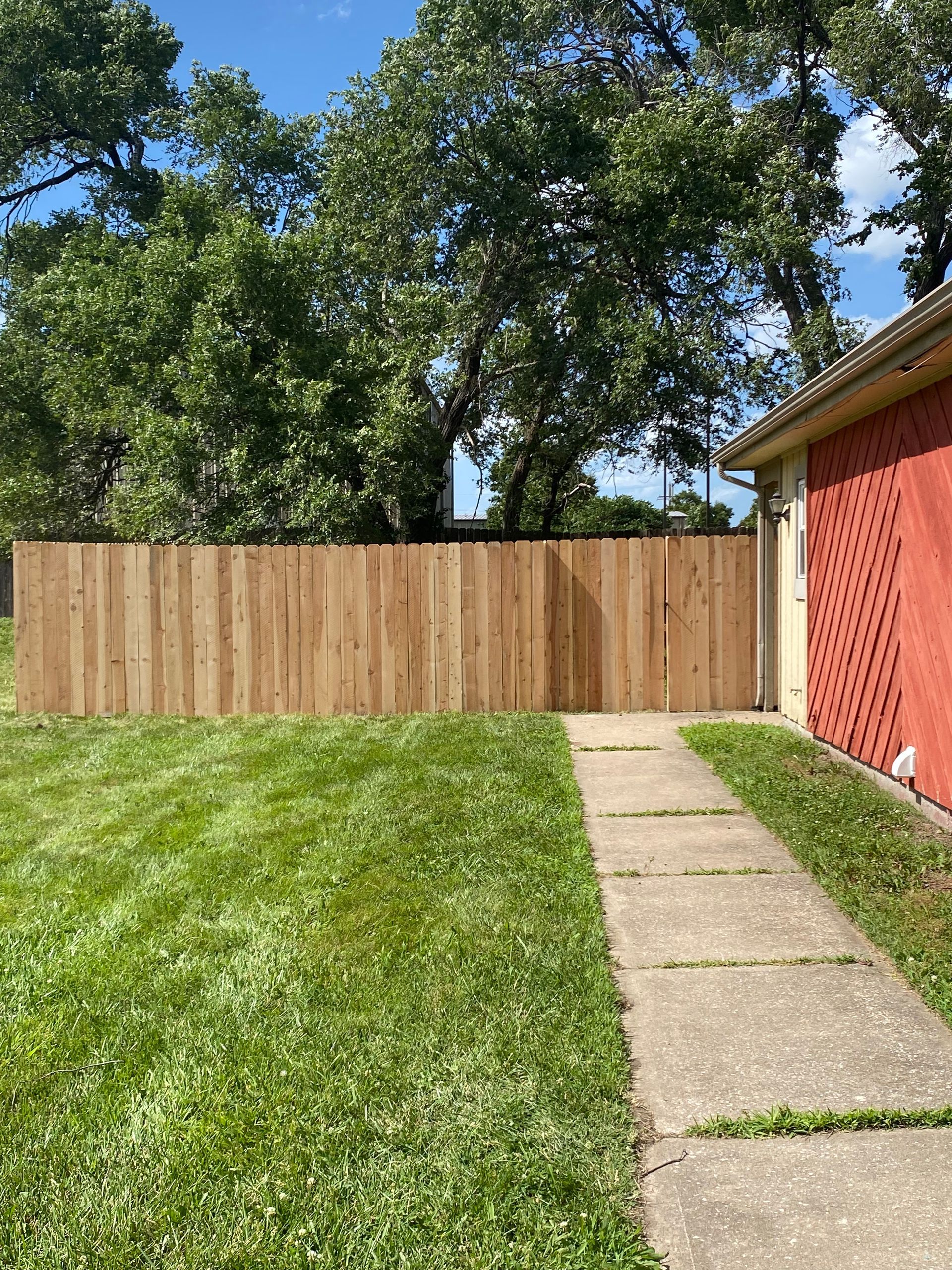 A wooden fence surrounds a lush green yard next to a sidewalk.