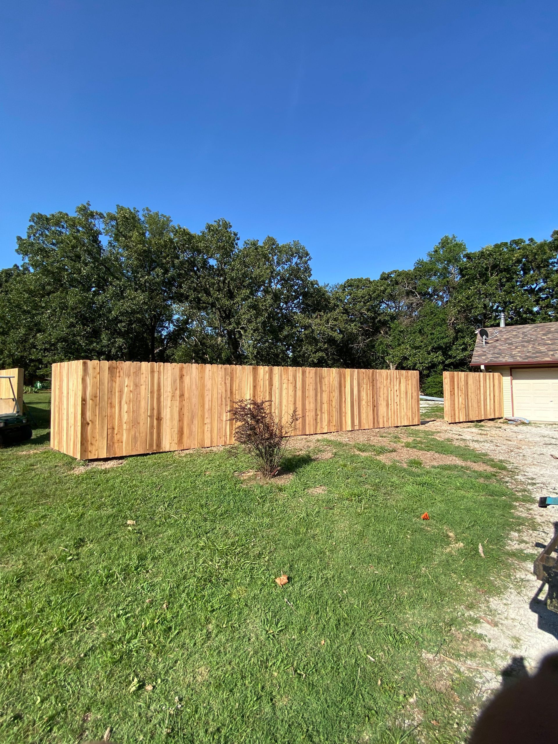 A wooden fence is sitting in the middle of a grassy field next to a house.