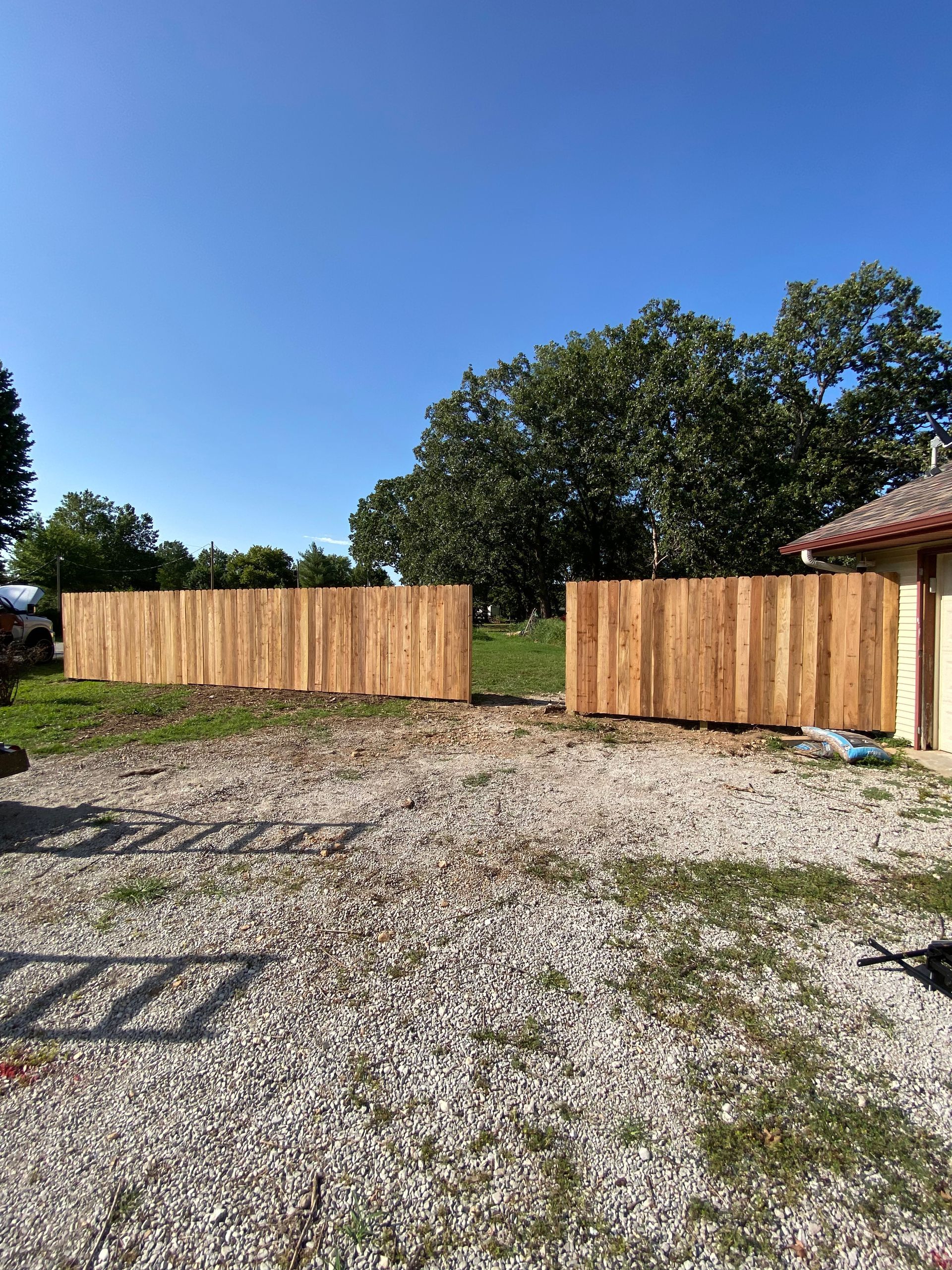 A wooden fence is sitting in the middle of a gravel driveway next to a house.