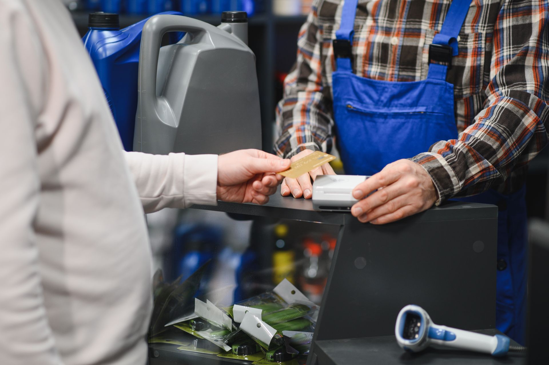 A person hands a credit card to a worker wearing blue overalls to make a payment at an auto supply store counter.