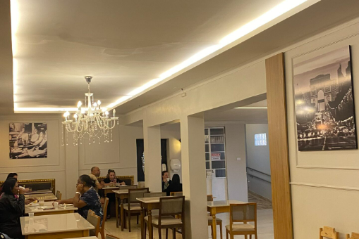 Interior de restaurante com clientes sentados às mesas. Lustres e obras de arte adornam as paredes.