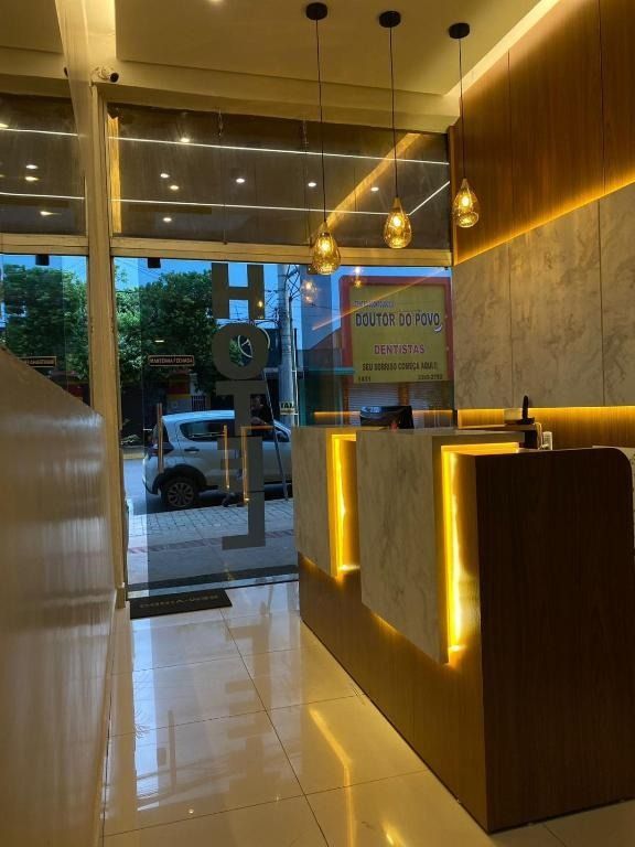 Área de recepção moderna com porta de vidro, balcões iluminados e luminárias pendentes.