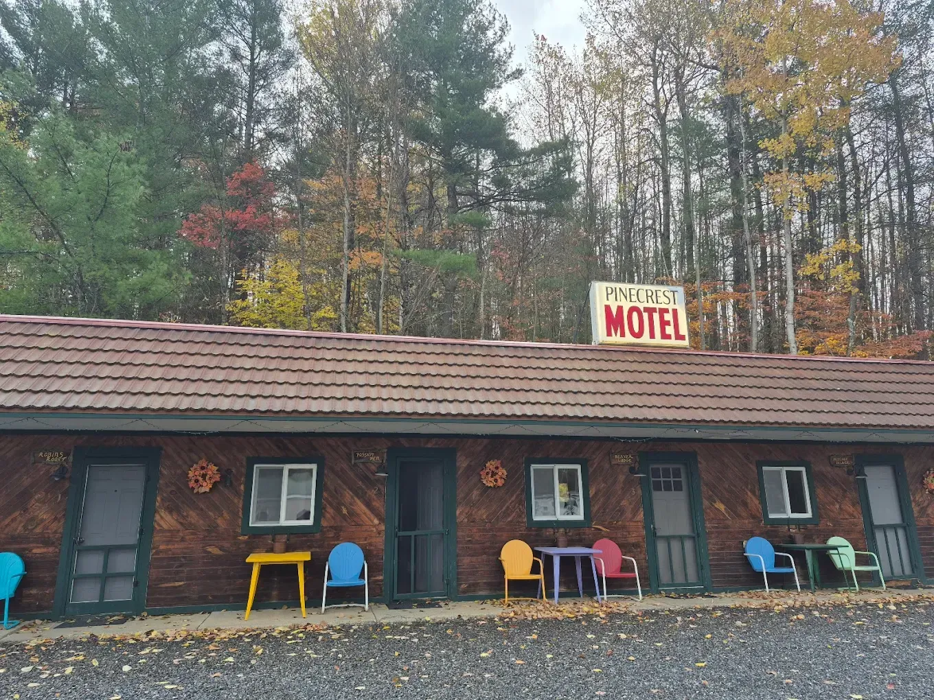 Small roadside motel with colorful chairs outside, set against autumn trees.
