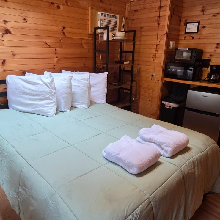 Cozy wooden cabin bedroom with a neatly made bed, white pillows, and folded towels on top