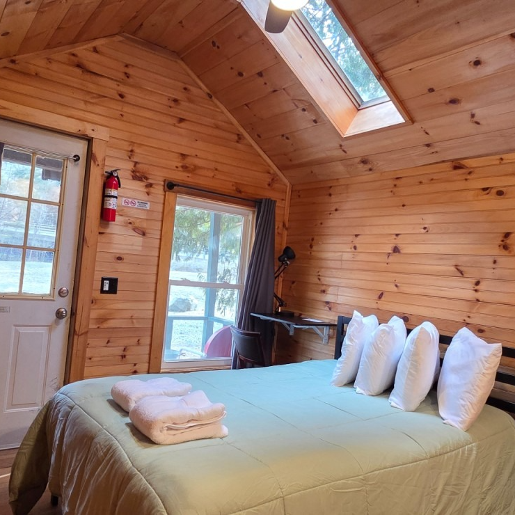 Cozy wood-paneled cabin bedroom with a bed, folded towels, skylight, and lake view through the window
