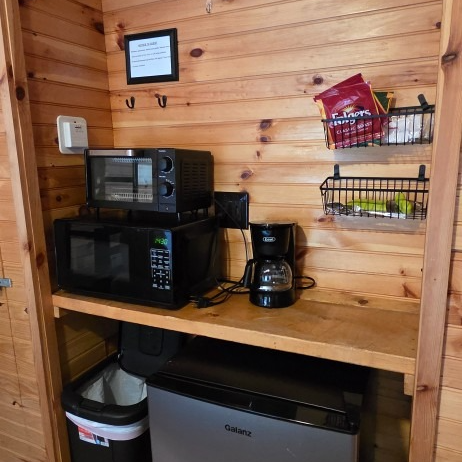 Wood-paneled kitchenette with microwave, coffee maker, mini fridge, and wall-mounted snack shelves.