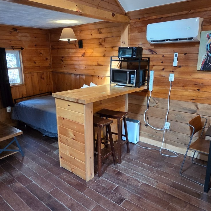 Cozy wood-paneled cabin room with a bed, desk, microwave, air conditioner, and small window