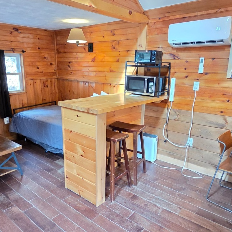 Cozy wood-paneled cabin room with bed, small table, microwave, and wall-mounted air conditioner