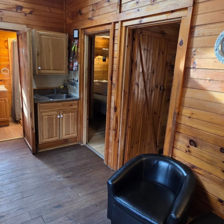 Wood-paneled cabin interior with a small cabinet, doorway, and black chair on a wooden floor