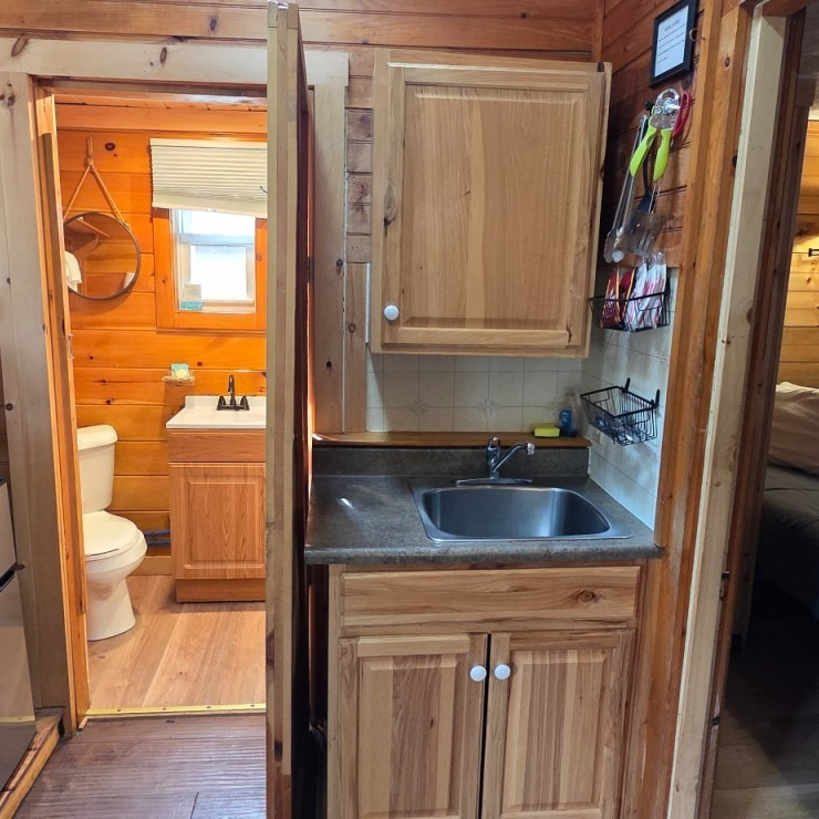 Small wood-paneled kitchenette with sink and cabinets beside an open doorway to a bathroom