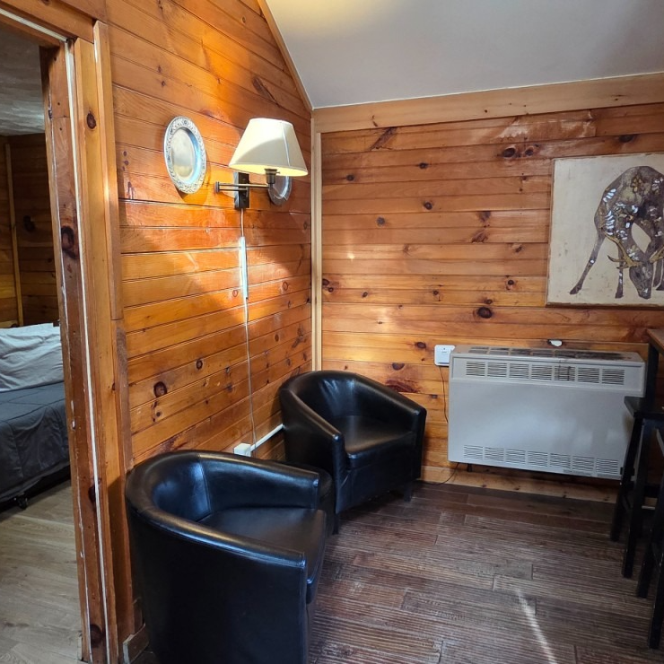 Wood-paneled room with two black chairs, wall lamp, round mirror, and a window air conditioner.