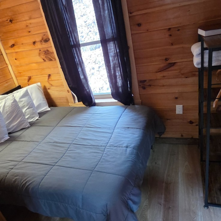 Cozy wood-paneled bedroom with a bed, gray bedding, and a window with dark curtains