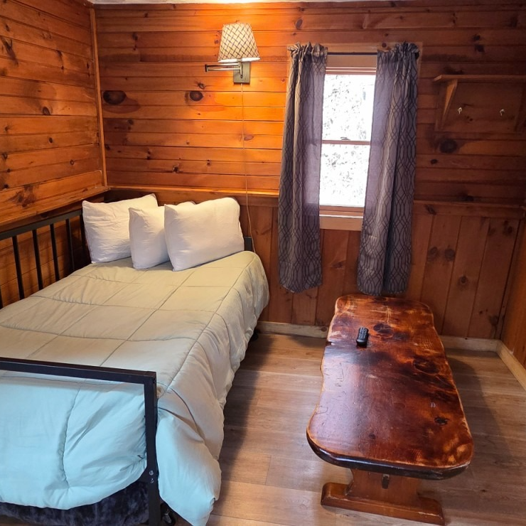 Cozy wood-paneled cabin bedroom with a twin bed, rustic bench, and window with curtains