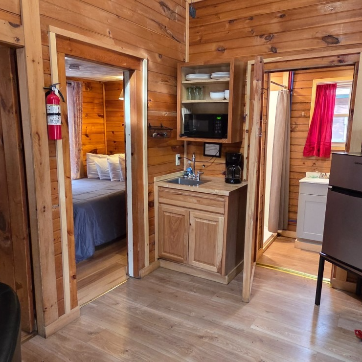 Wood-paneled cabin room with two doorways, kitchenette, and a bedroom visible through one doorway