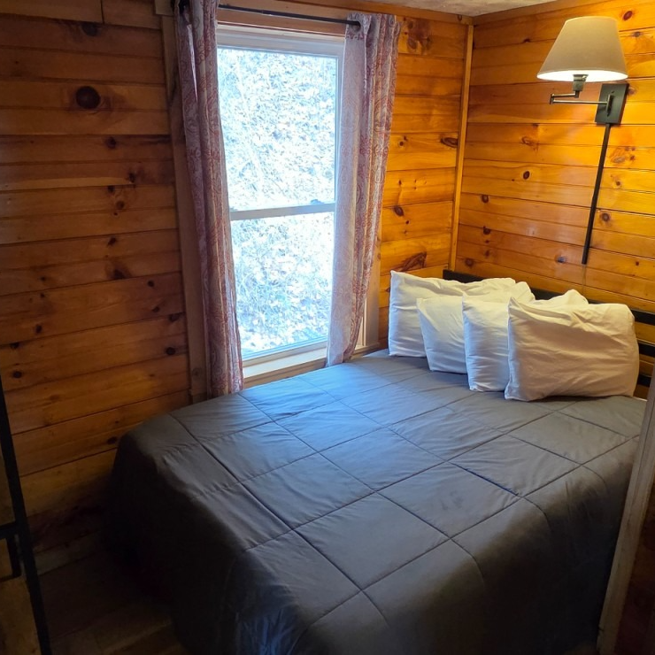 Cozy wood-paneled bedroom with gray bed, white pillows, and a window beside a floor lamp.