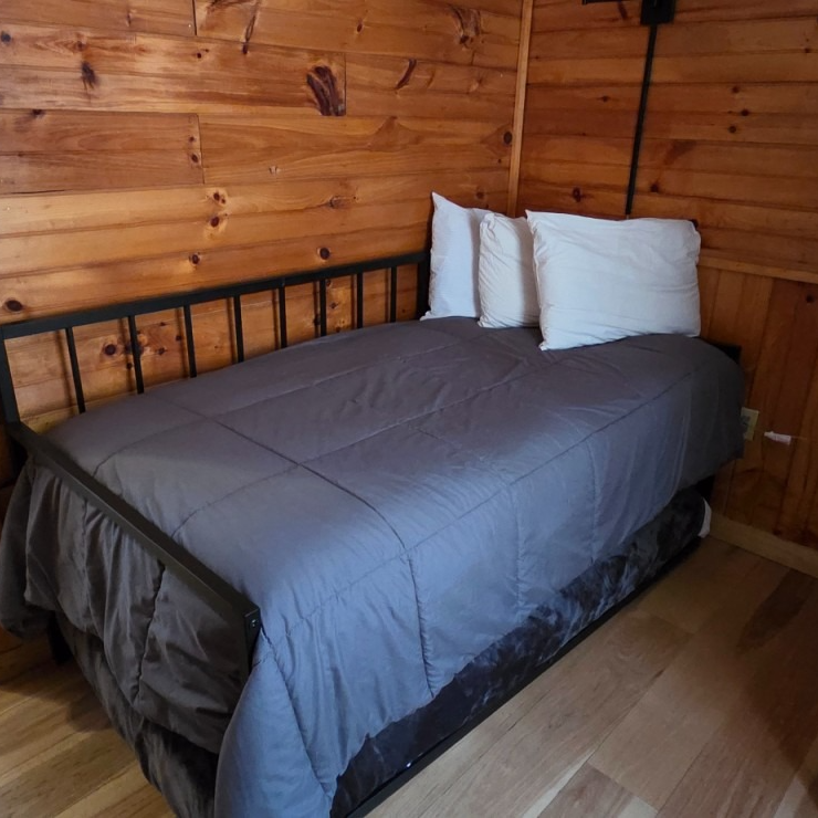 Single bed with gray bedding and white pillows in a wooden-paneled cabin room
