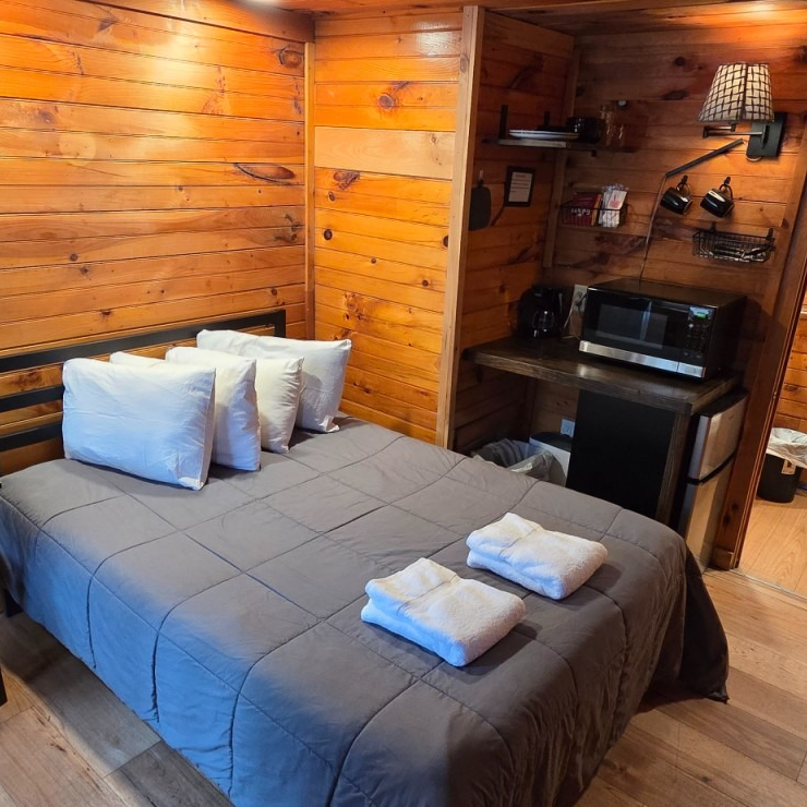Cozy wooden cabin bedroom with a gray bedspread, white pillows, and a small desk area