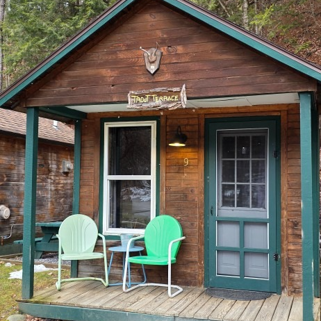 Small rustic cabin porch with two mint-green chairs and a blue door