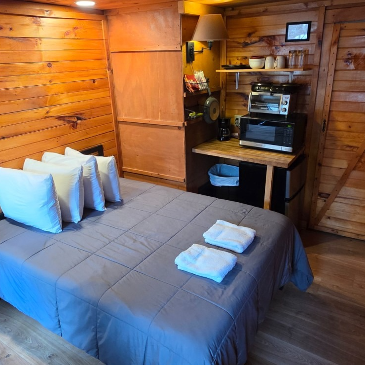 Cozy wood-paneled bedroom with queen bed, folded towels, and a small kitchenette nook