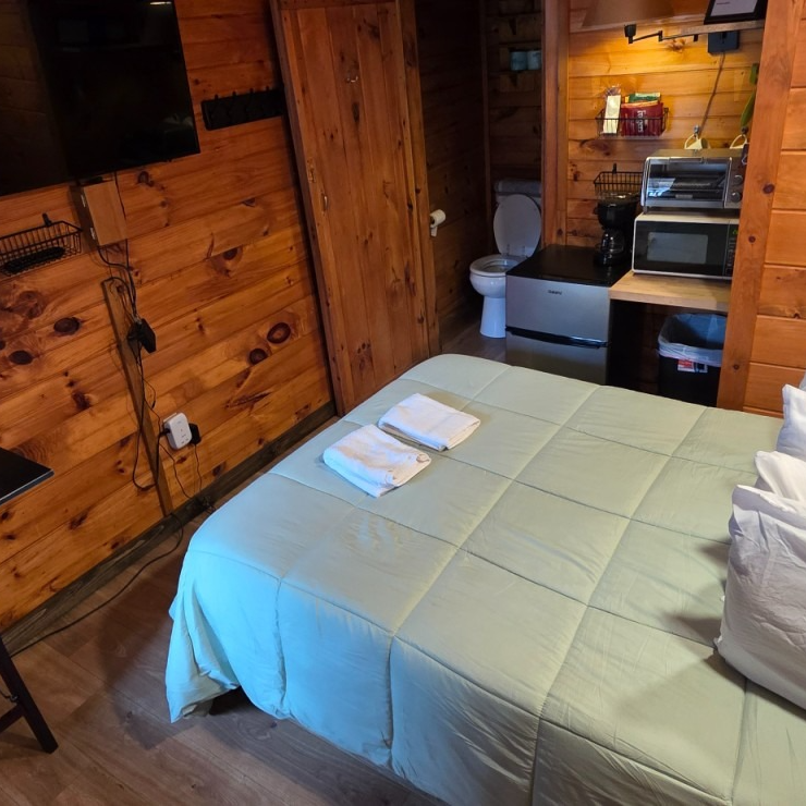 Wood-paneled cabin bedroom with a bed, folded towels, and a small bathroom nook with a toilet and sink.