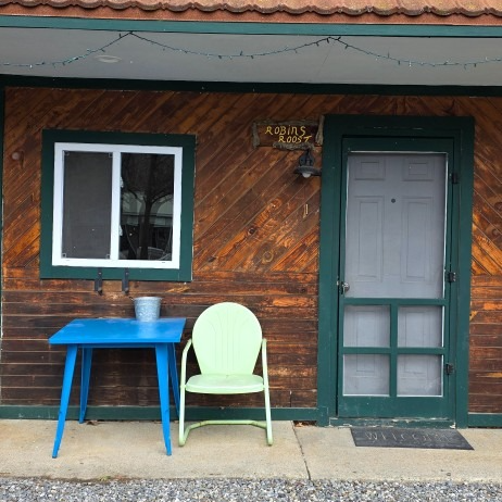 Blue table and green chair outside a rustic cabin door and window