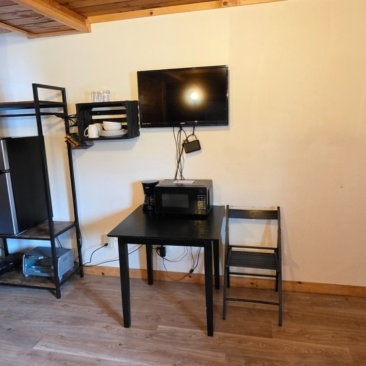 Small room with wall-mounted TV, black desk with printer, chair, and shelving on a wooden floor.