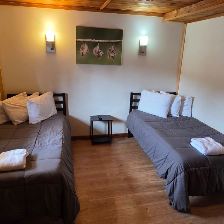 Cozy bedroom with two twin beds, wood floor, wall lamps, and a framed picture above the headboard.