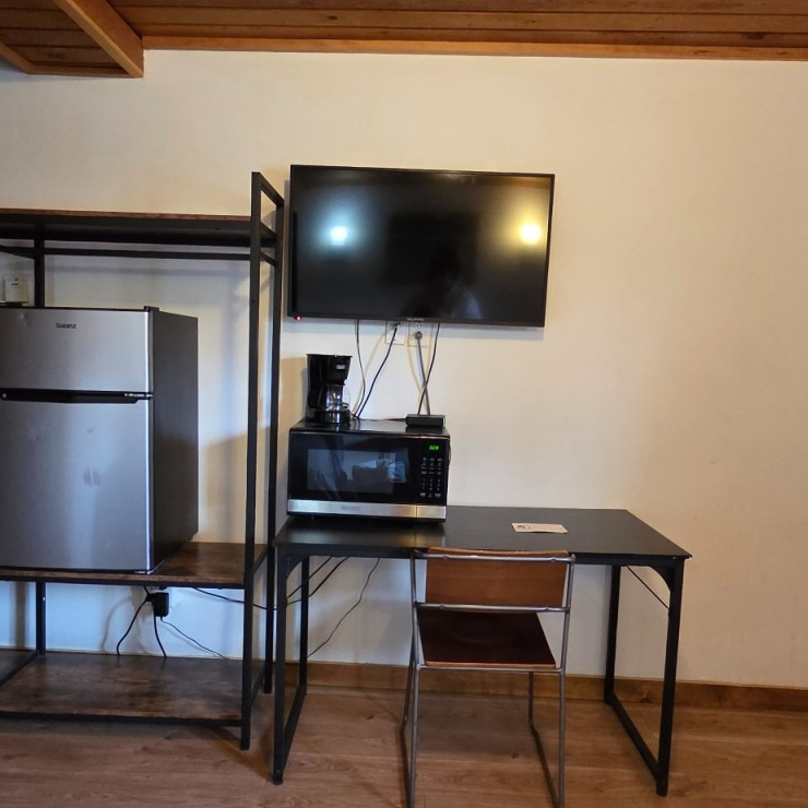 Small room with a TV, mini fridge, microwave, desk, chair, and black metal shelving unit.