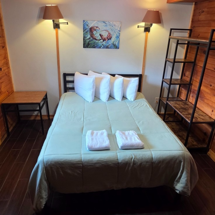 Cozy bedroom with a neatly made bed, wall lamps, wooden furniture, and folded towels on the bed