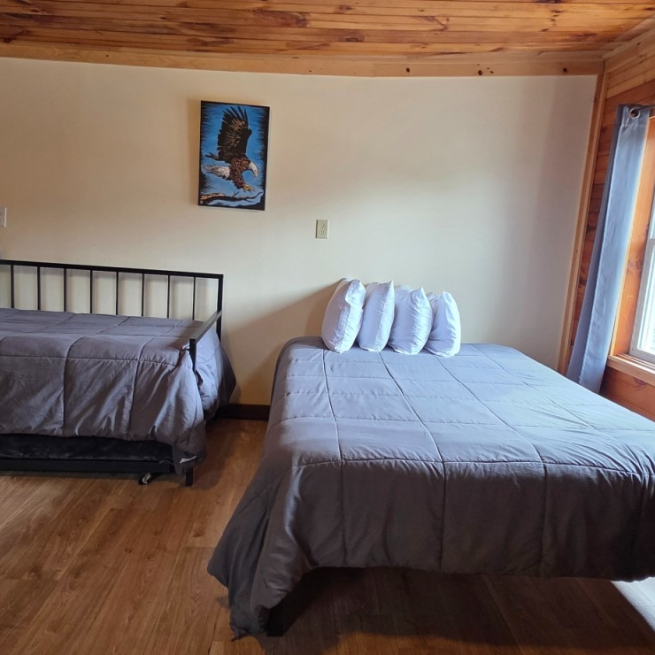Two made beds in a wood-paneled bedroom, one twin and one larger bed by a window.