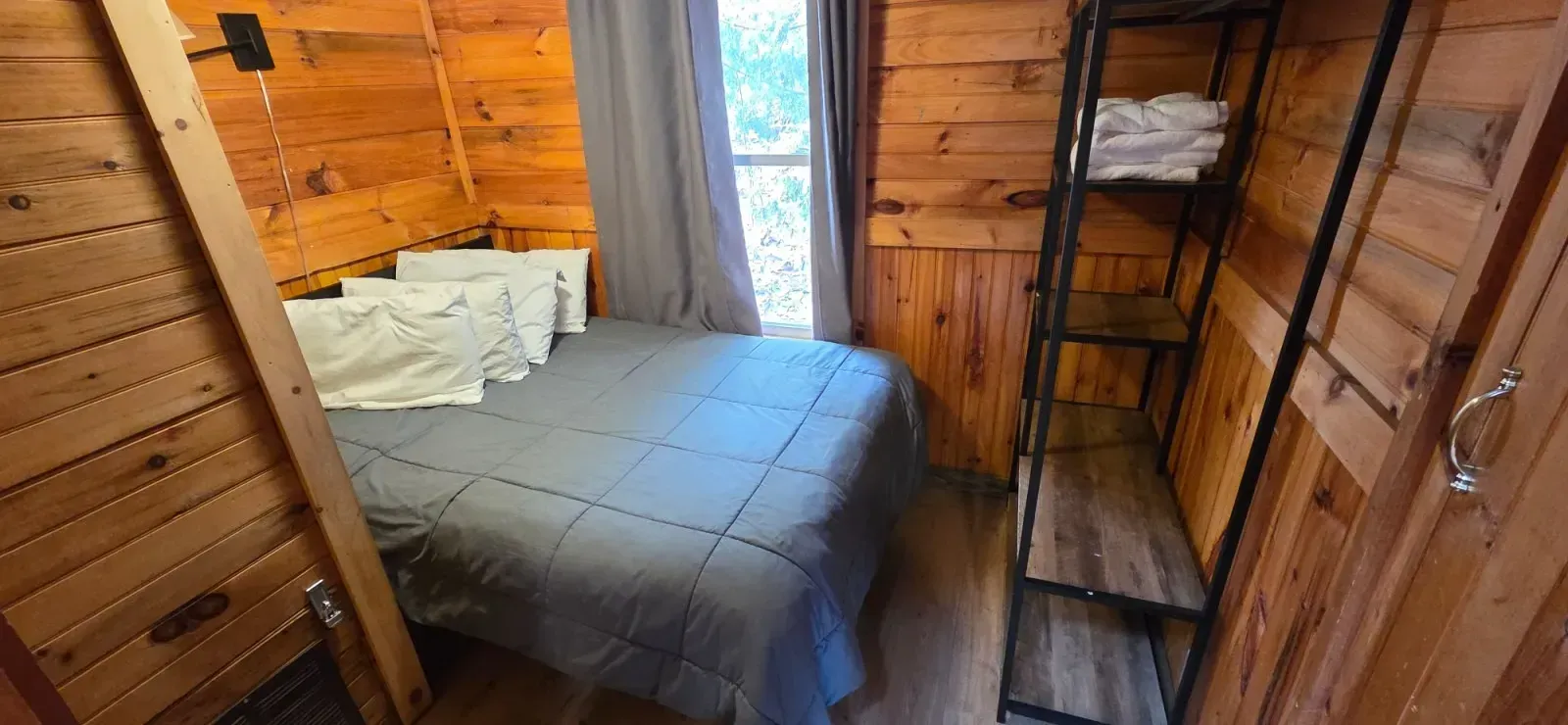 Small wooden cabin bedroom with a bed, window curtains, and a bunk bed against the wall.