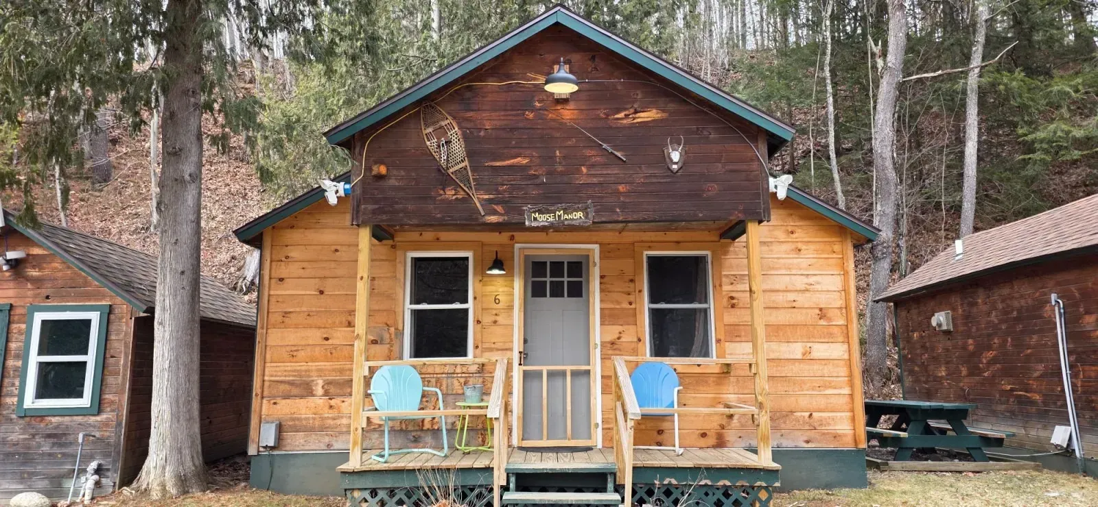 Rustic wooden cabin with a small porch, two chairs, and trees in the background
