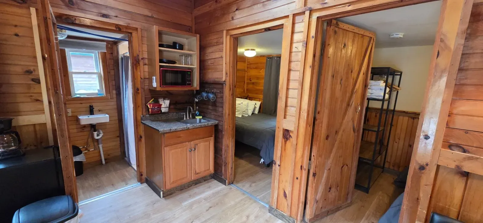 Wood-paneled cabin interior with kitchenette, doorway to a bedroom, and stairs on the right.