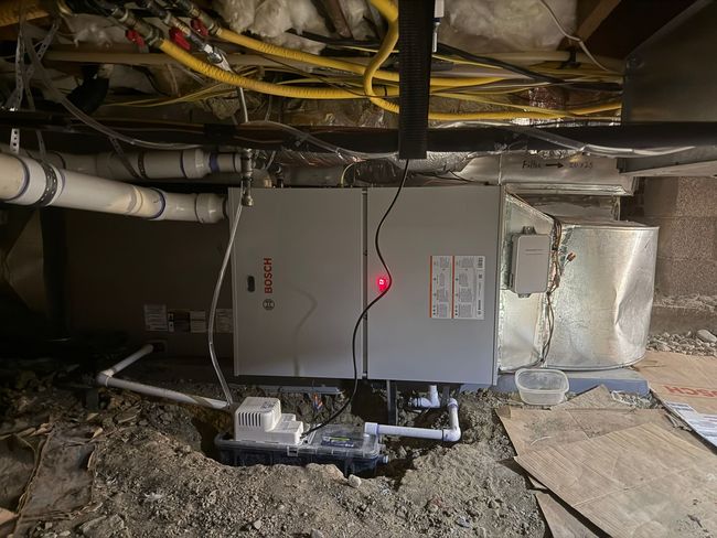 Gray HVAC unit in a basement crawlspace with exposed pipes, ducts, and insulation.