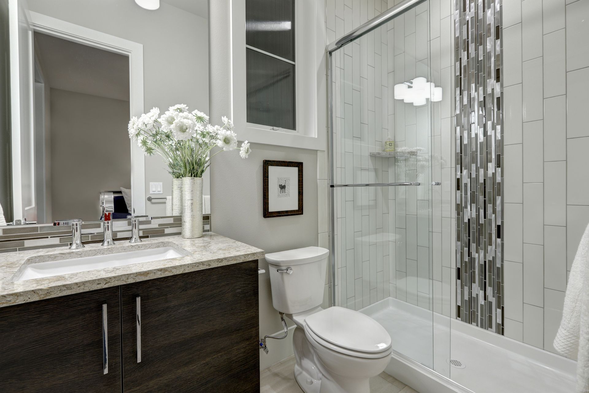 Modern bathroom with dark vanity, white toilet, glass shower, and marble tile accents