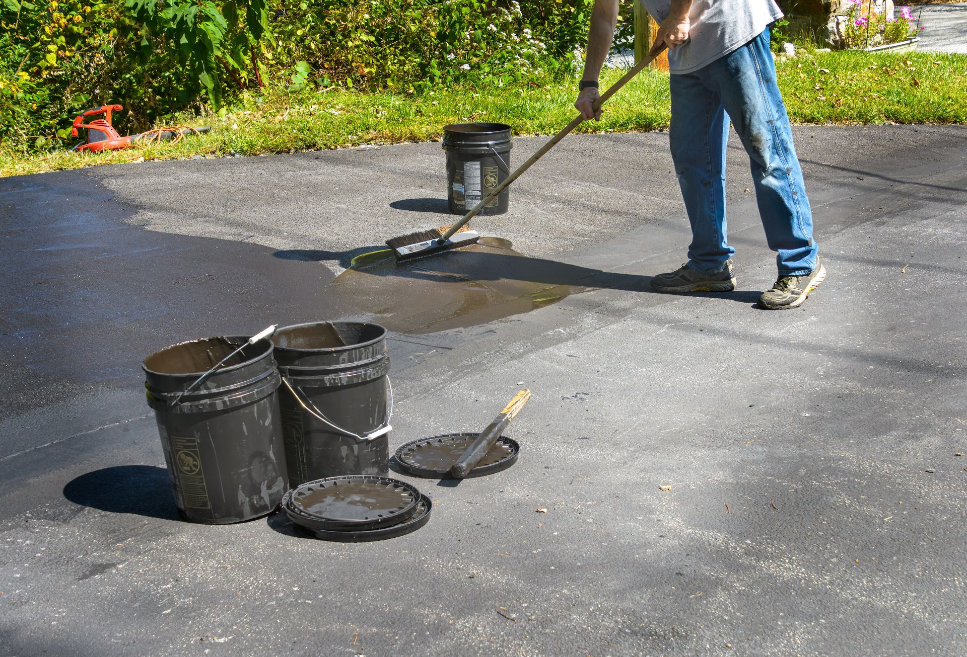 Person spreading black sealant on a driveway with buckets and tools nearby Person spreading black sealant on a driveway with buckets and tools nearby