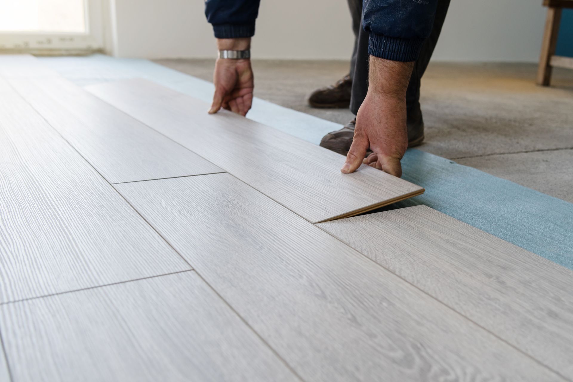 Person installing light wood flooring in a room, lifting a plank during installation.