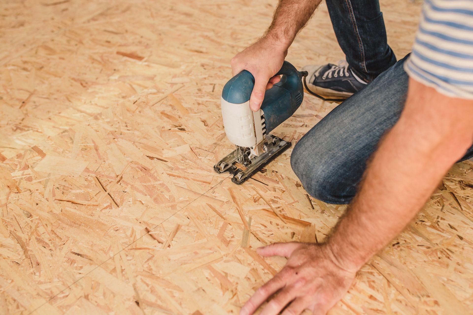 Person using a jigsaw to cut plywood flooring on a construction site