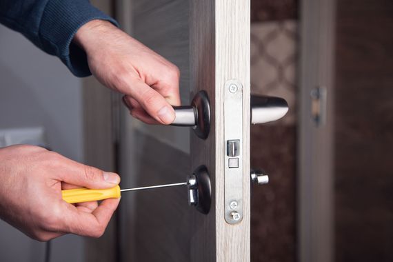 Hands using a yellow screwdriver to unlock a door handle on a white door Hands using a yellow screwdriver to unlock a door handle on a white door