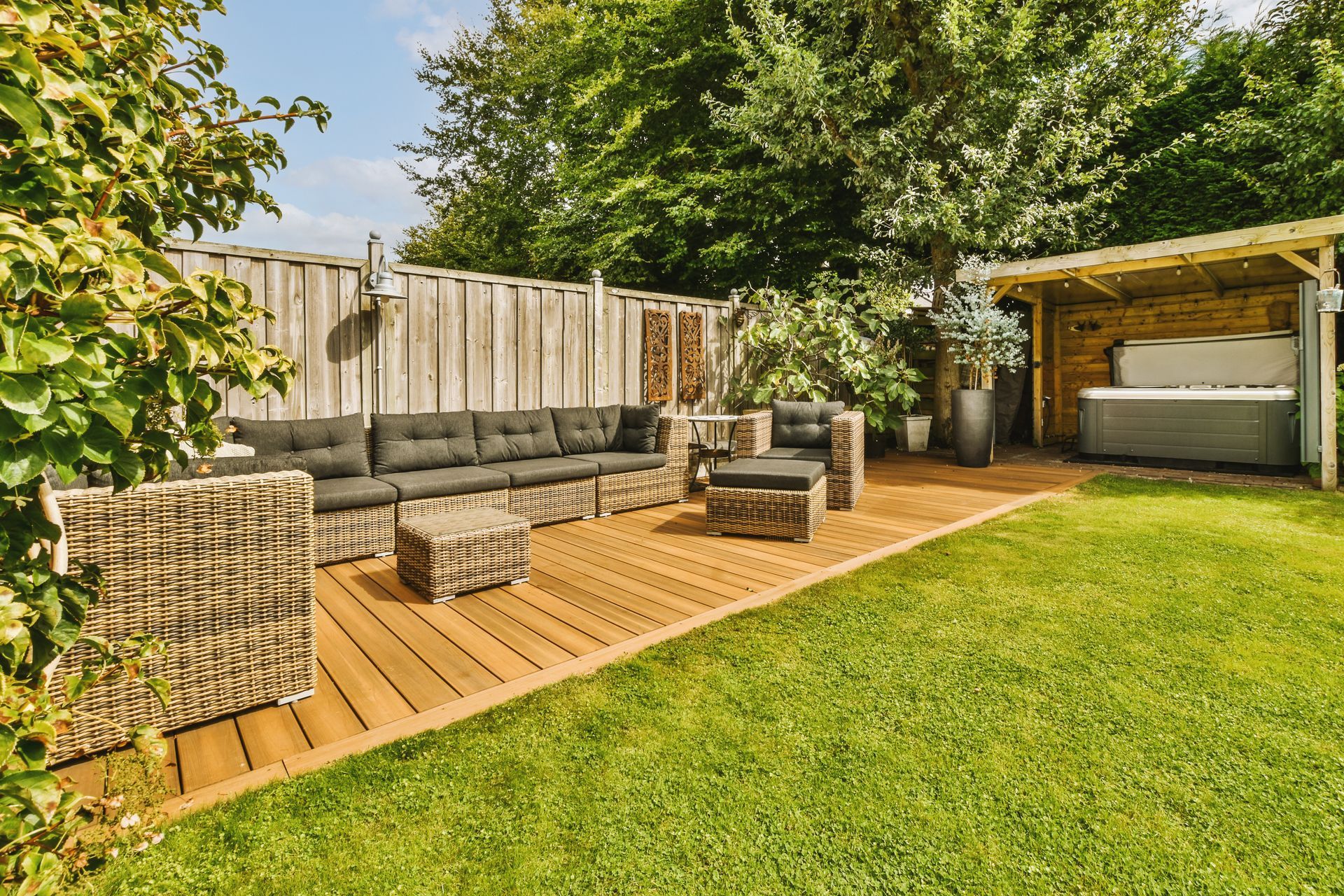 Backyard patio with wooden deck, outdoor seating, and green lawn beside a fenced garden area Backyard patio with wooden deck, outdoor seating, and green lawn beside a fenced garden area