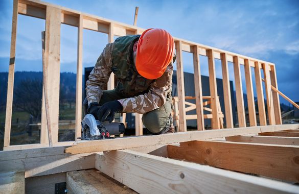 Construction worker in orange hard hat nailing wooden framing at a building site Construction worker in orange hard hat nailing wooden framing at a building site