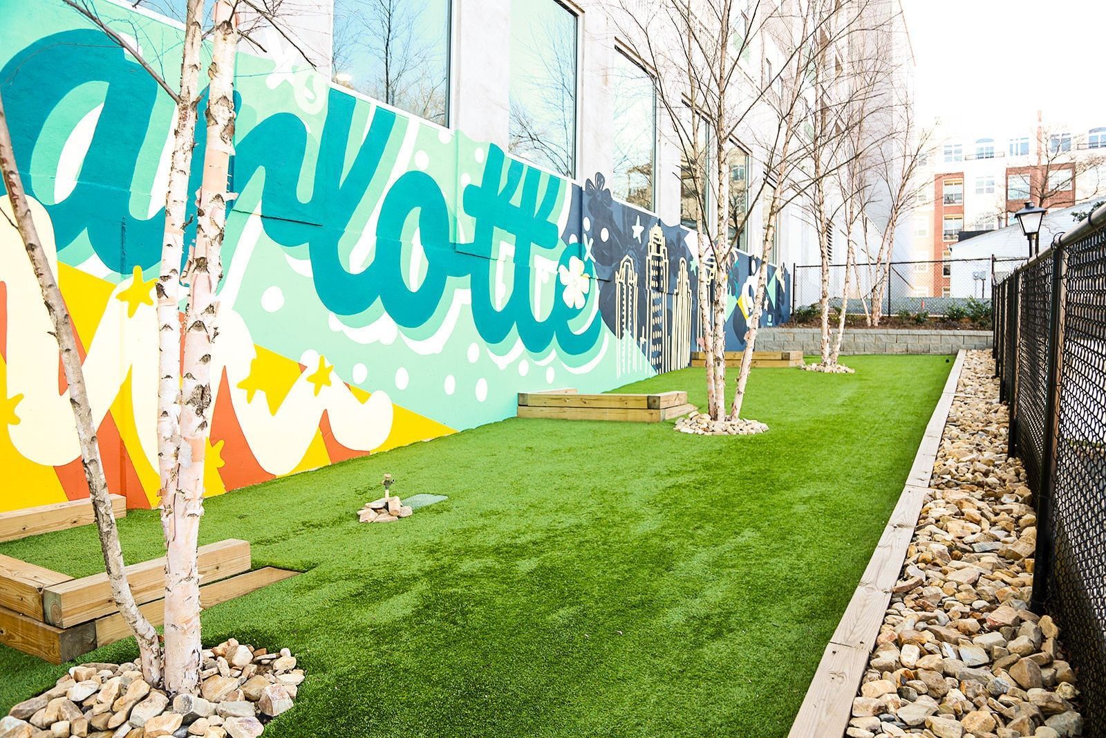 Outdoor area with artificial turf, birch trees, and a colorful mural on a wall.