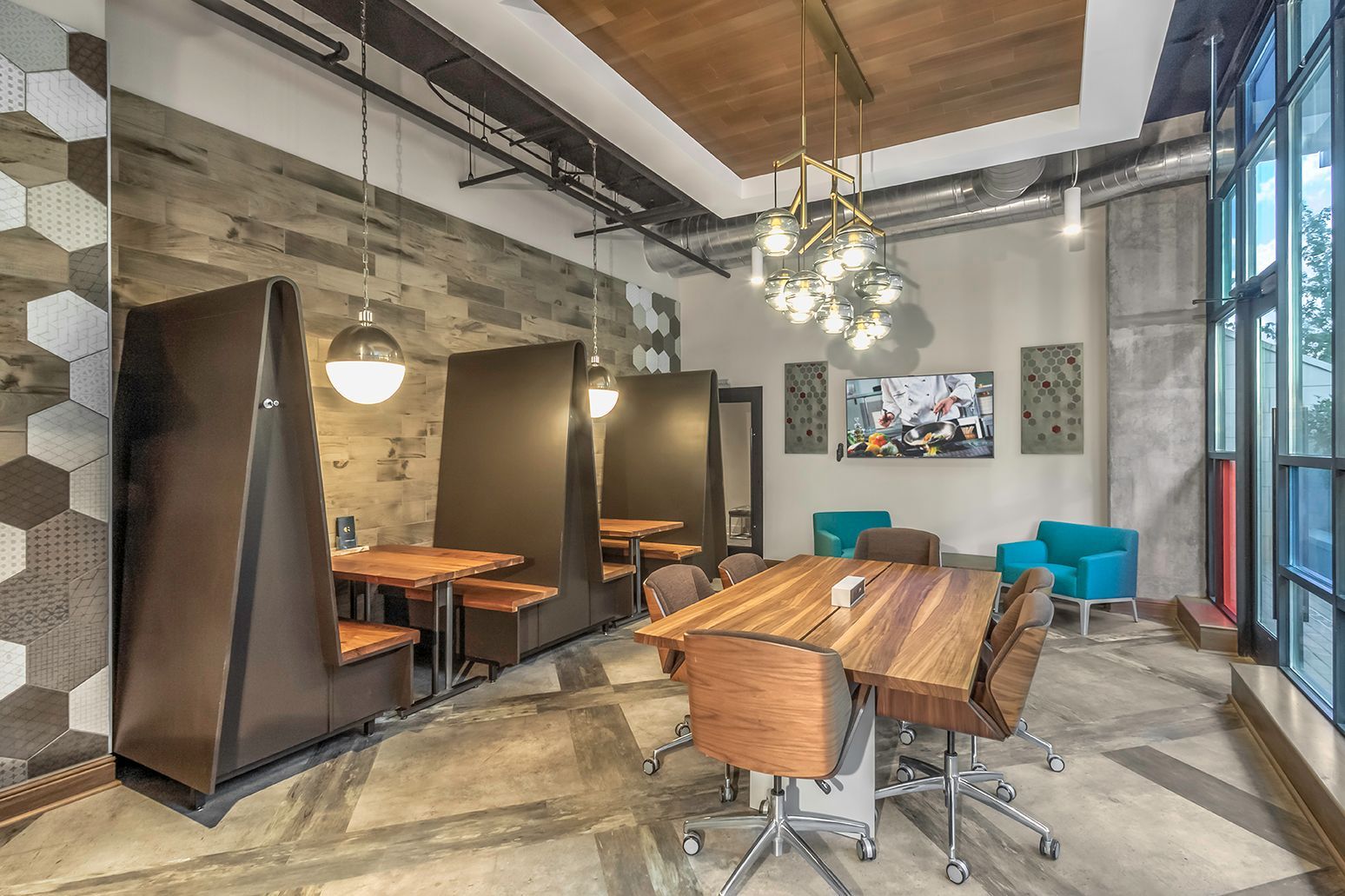 Modern communal lounge with booth seating, a large wooden table, and floor-to-ceiling windows.