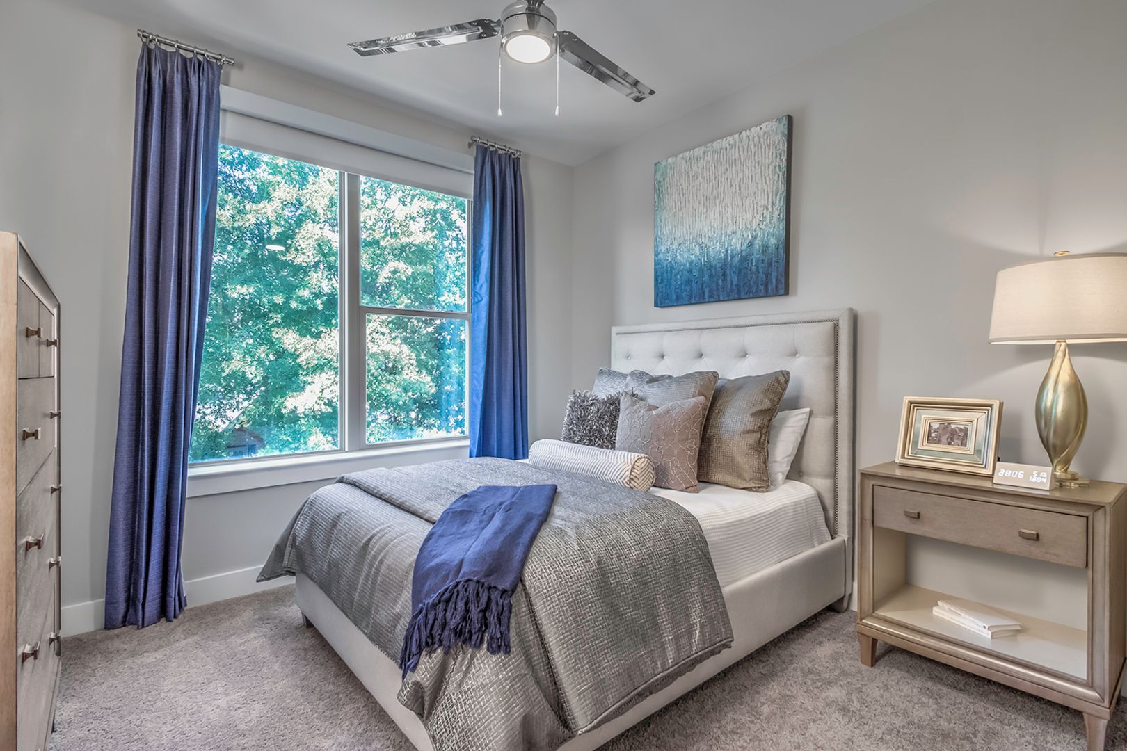 Bedroom in a modern apartment with a tufted headboard, gray bedding, and blue curtains.